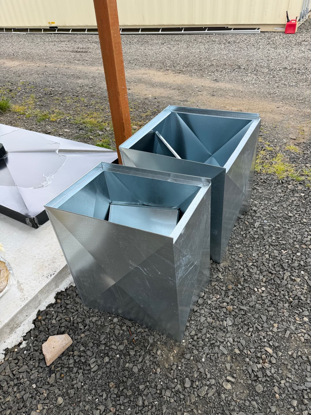 Two metallic, angular containers on gravel ground, showcasing industrial design.