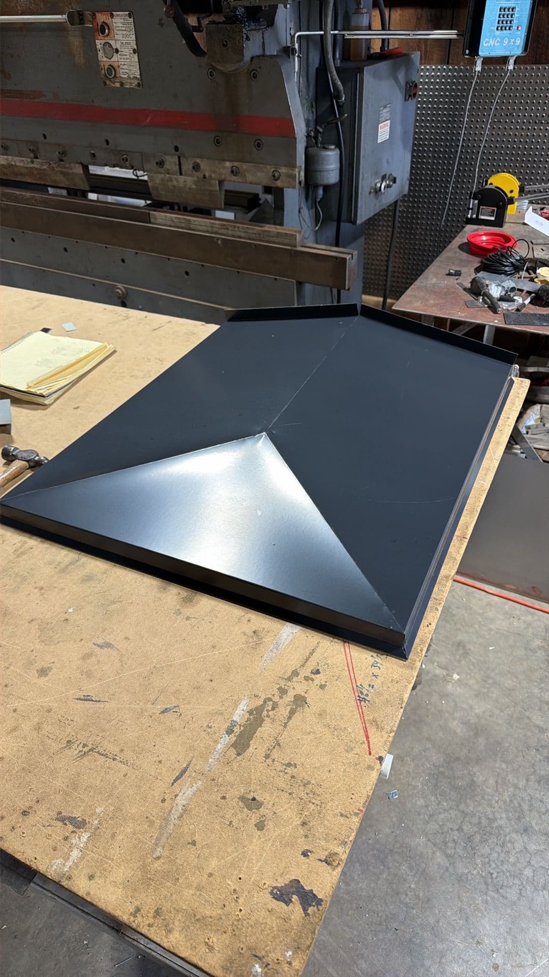Metal sheet with a pyramid-shaped design on a workshop table, surrounded by tools.
