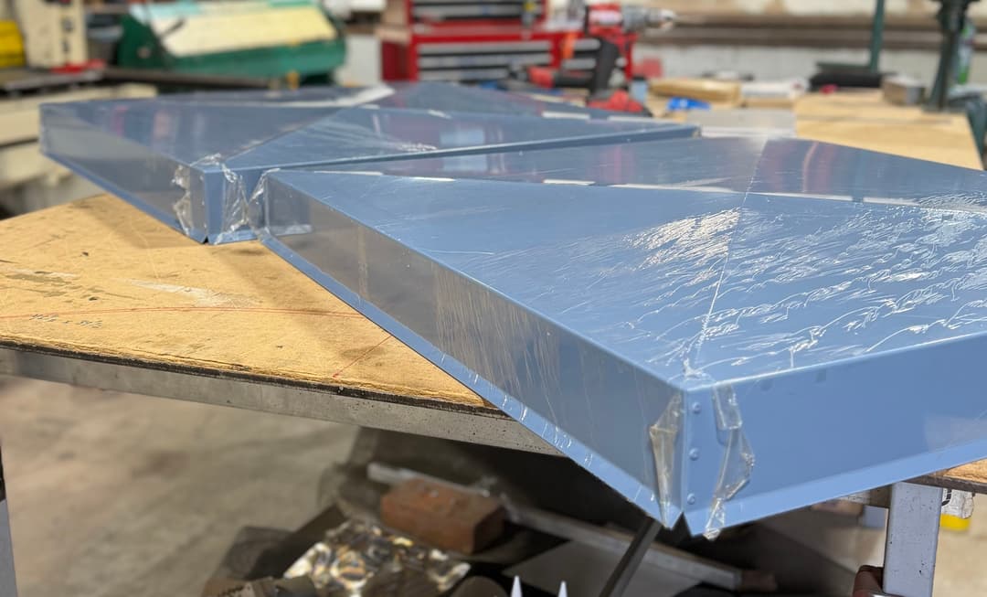 Newly wrapped blue metal panels on a workbench in a manufacturing workshop.