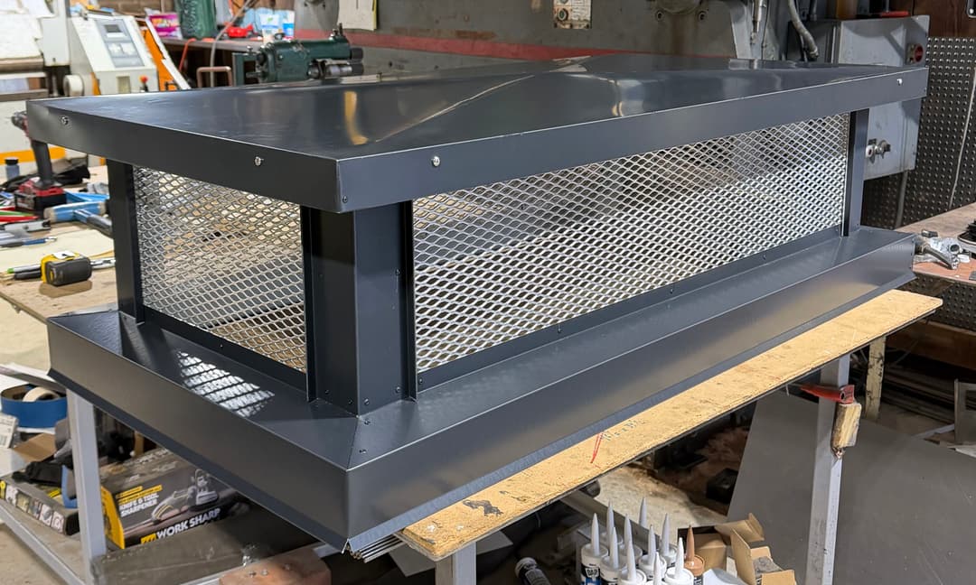 Industrial metal vent cover with mesh sides design, placed on a workbench in a workshop.