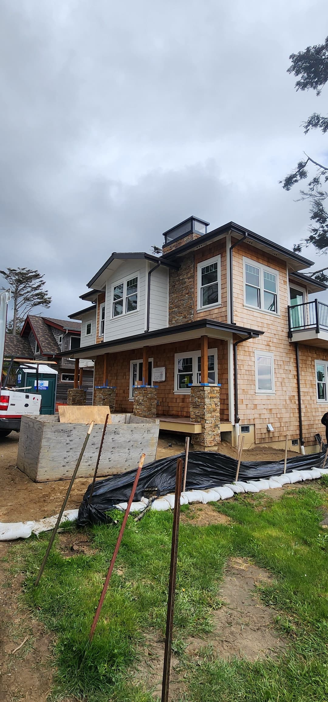 Newly constructed two-story house with stone accents and modern windows, under cloudy sky.