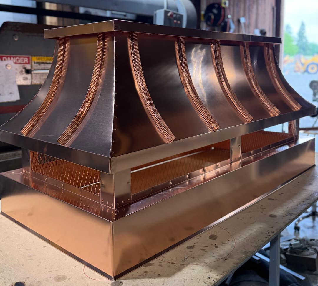 Copper hood range cover showcasing intricate design and craftsmanship in a workshop setting.