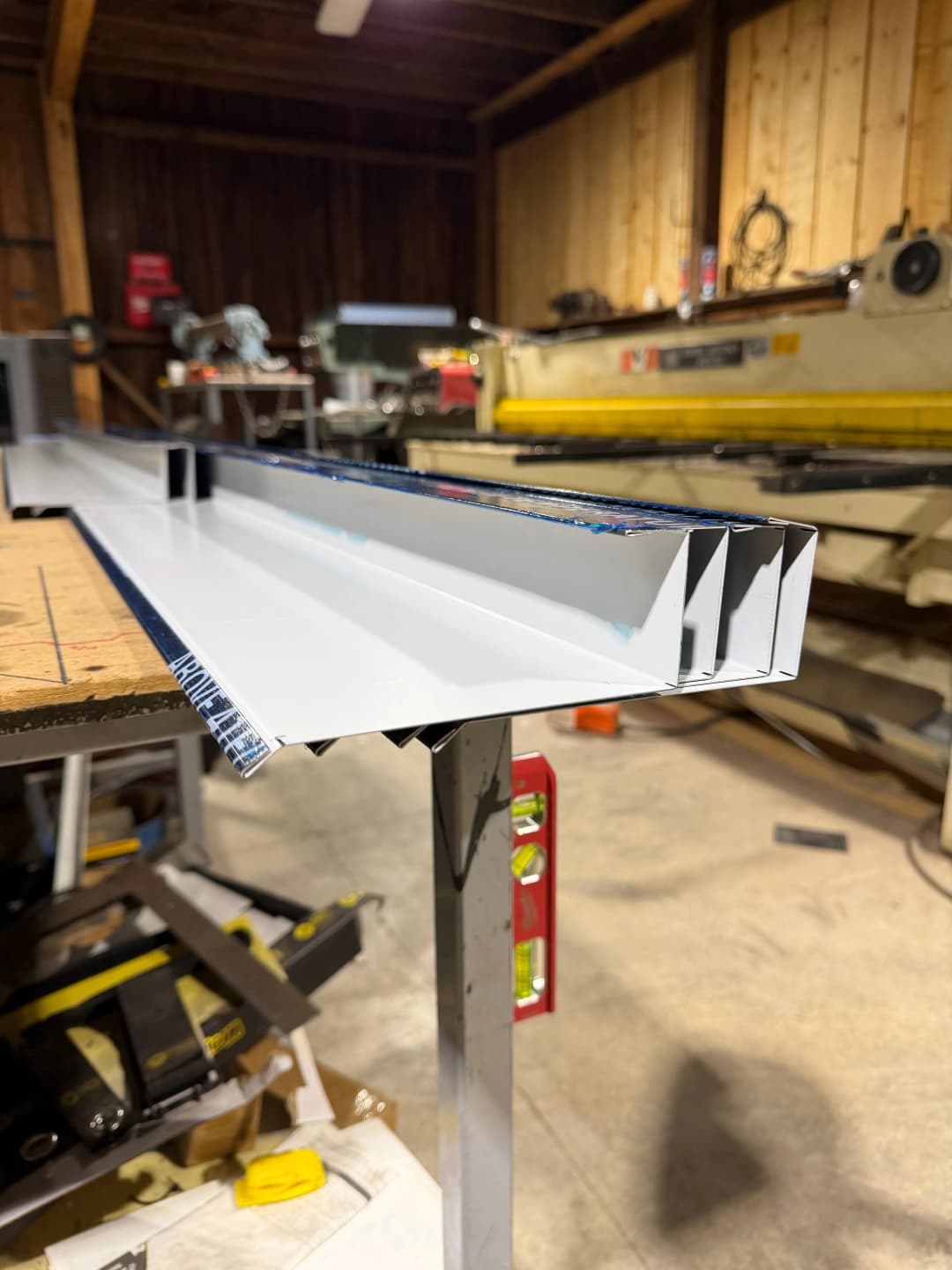 Metal roofing panel on a workbench in a workshop with machinery in the background.
