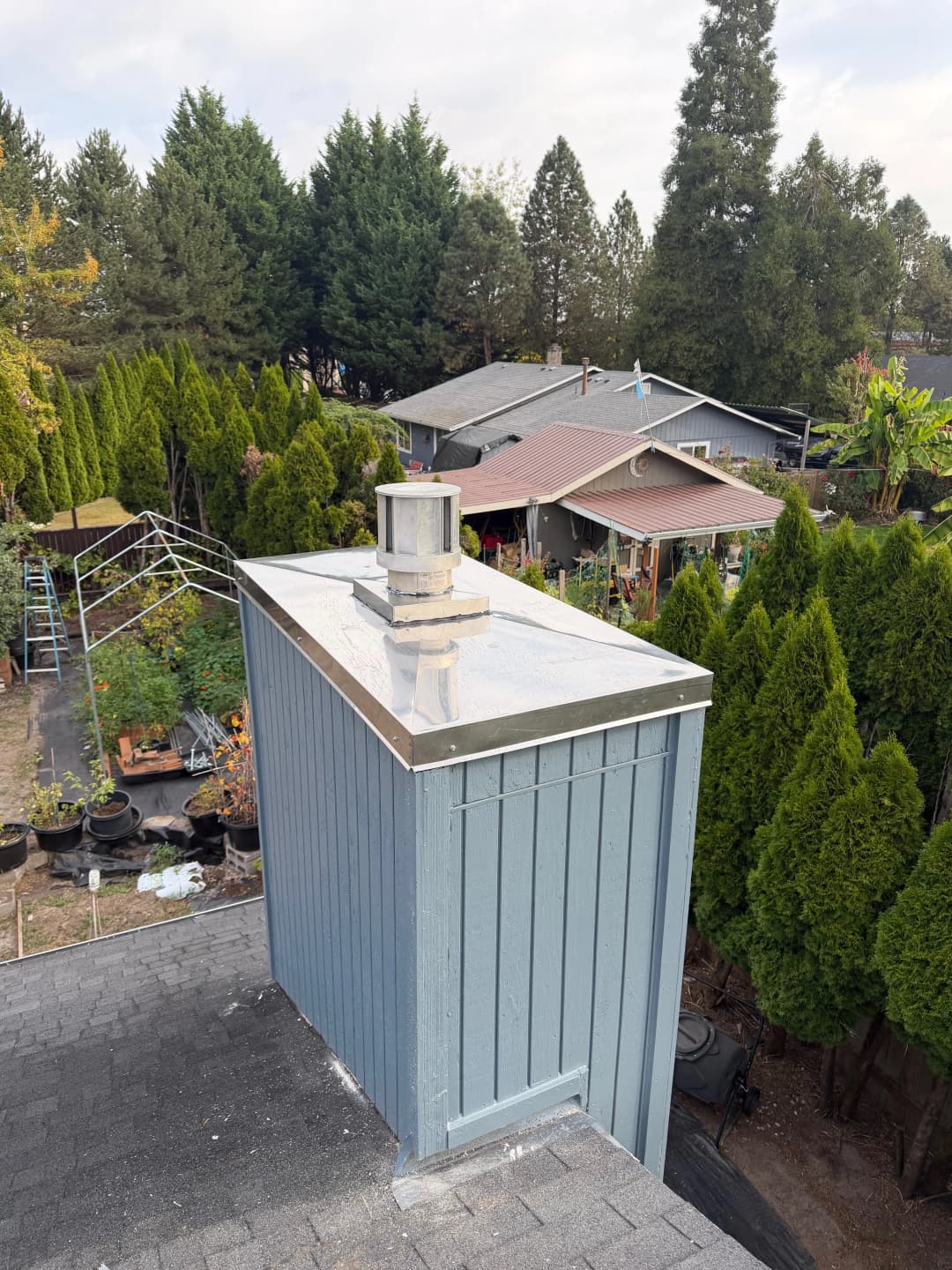 Blue chimney atop a roof overlooking a lush backyard with trees and gardens.