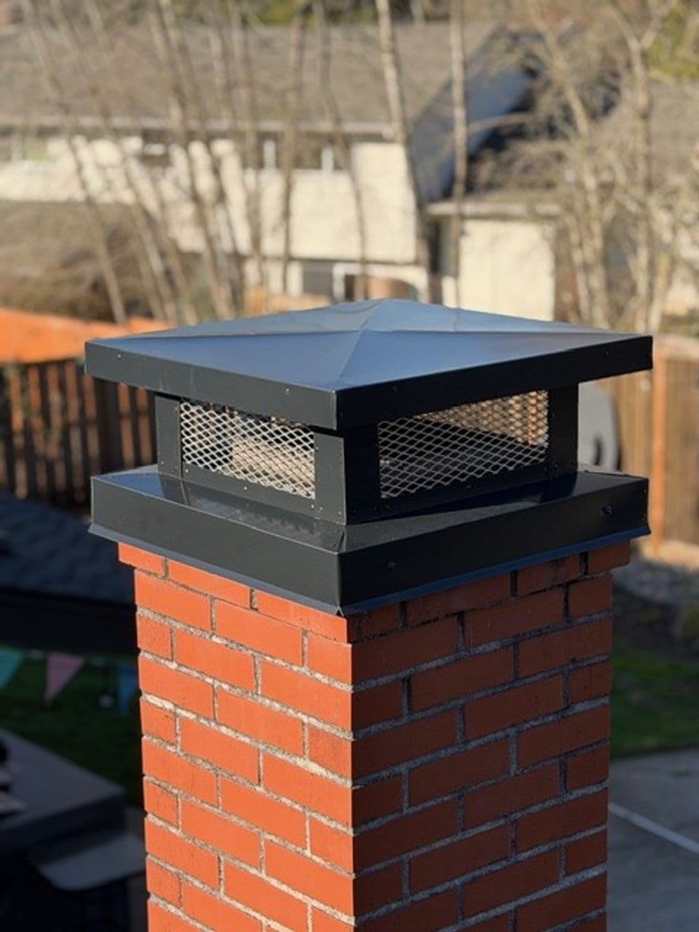Chimney cap atop a brick chimney, designed for ventilation and protection.