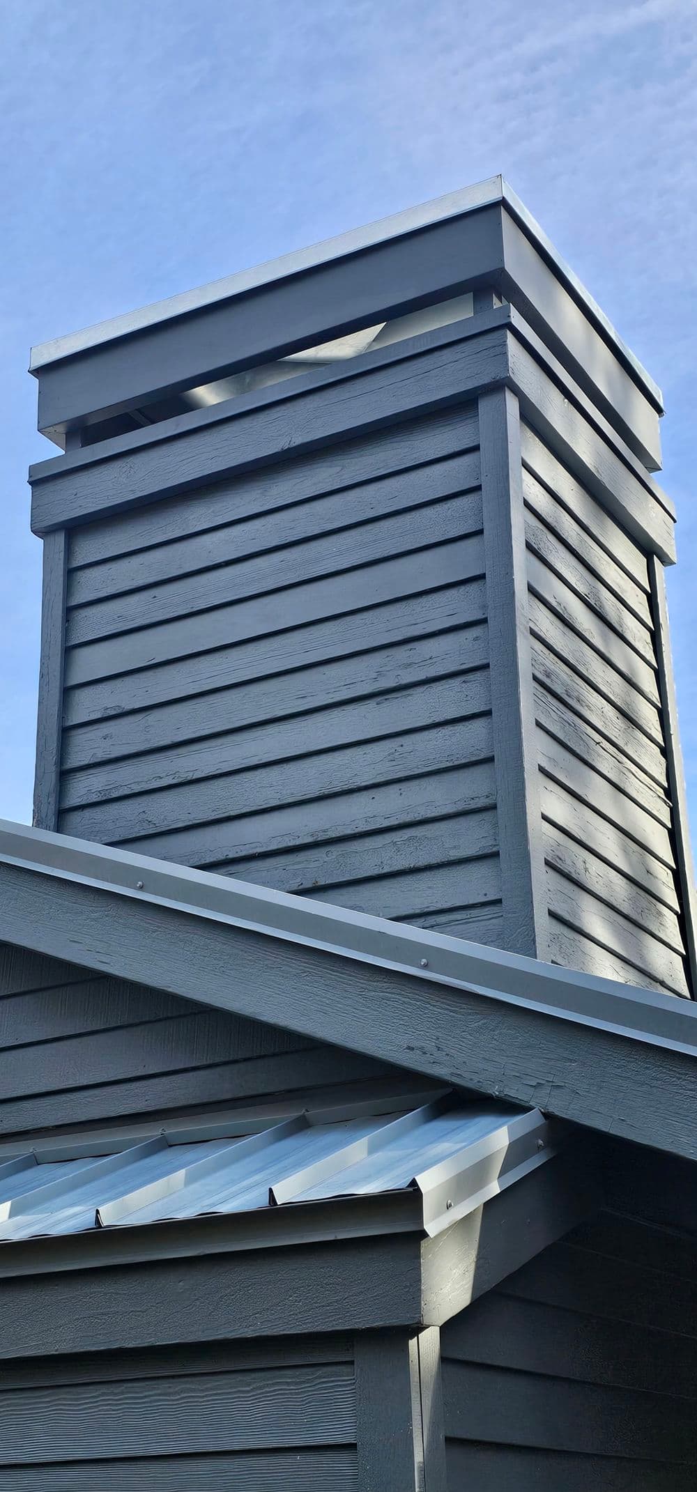 Dark wooden chimney atop a modern building against a clear blue sky.
