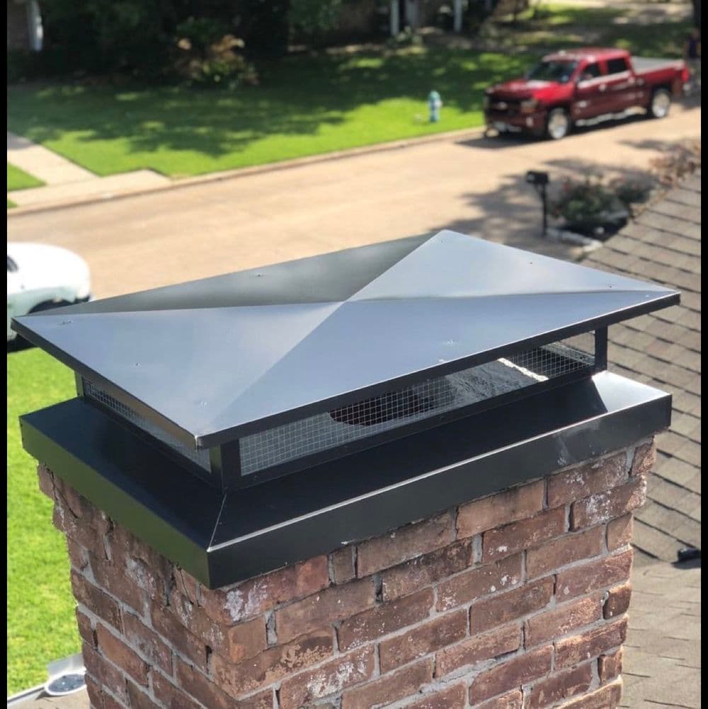 Chimney cap on a brick chimney with mesh screen, set against a green lawn background.