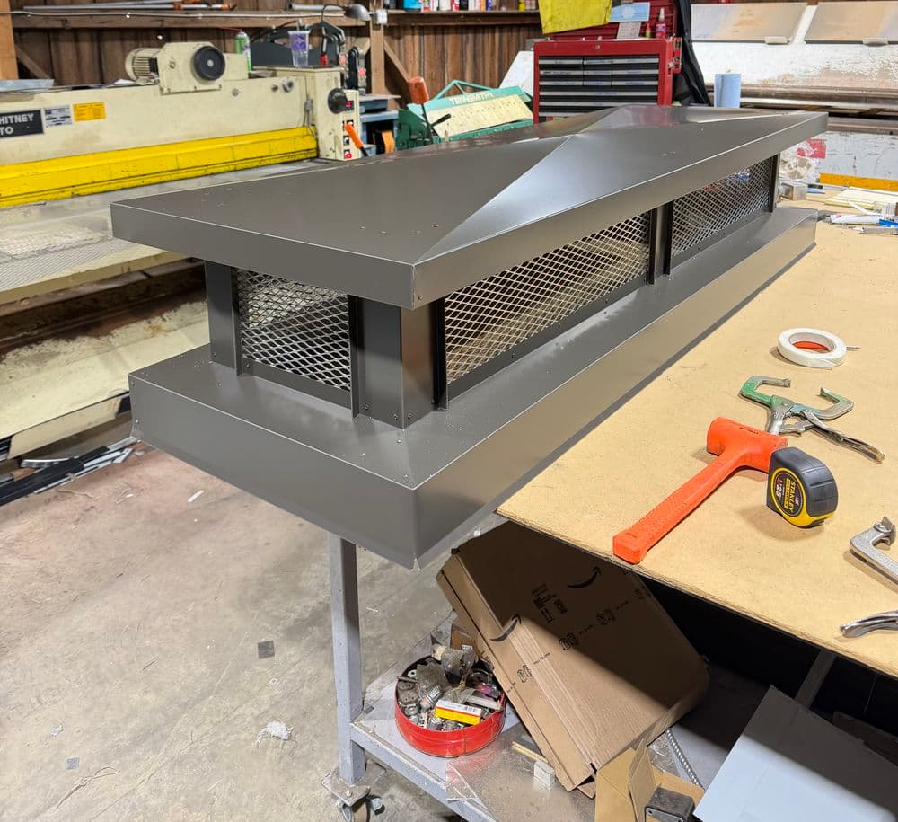 Metal exhaust hood on a workbench, featuring ventilation grilles and tools nearby.