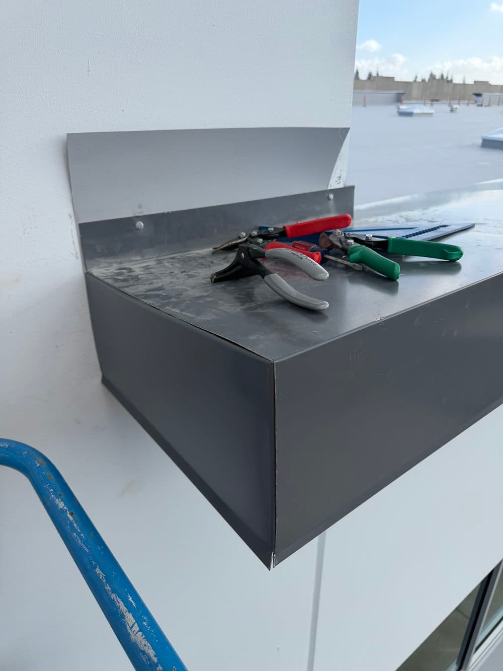 Metal ledge with sheet metal tools including pliers and scissors on a construction site.