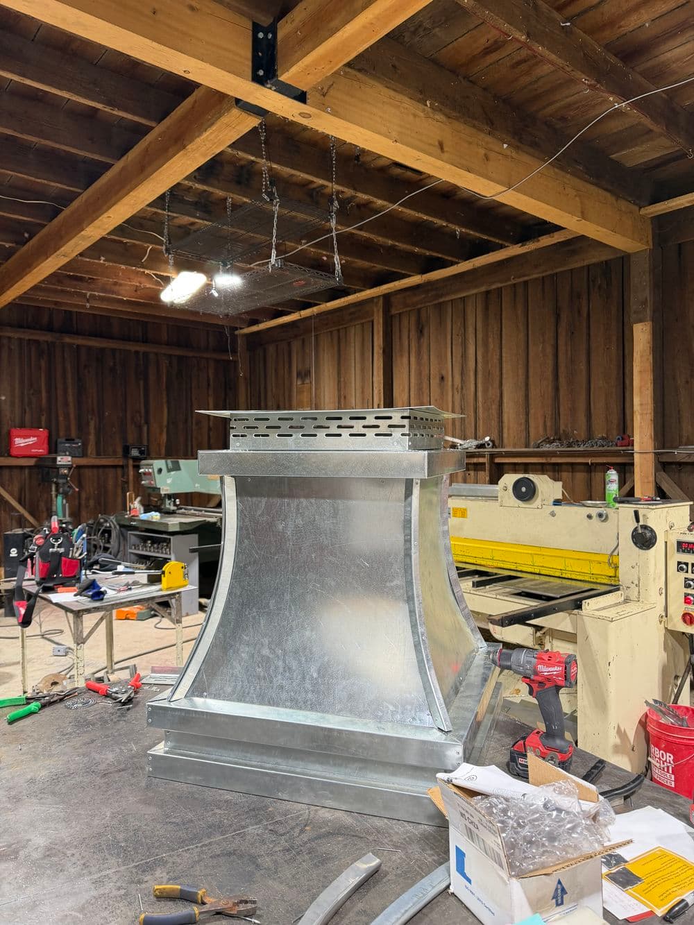Metal ductwork installation in a workshop with machinery and tools visible.