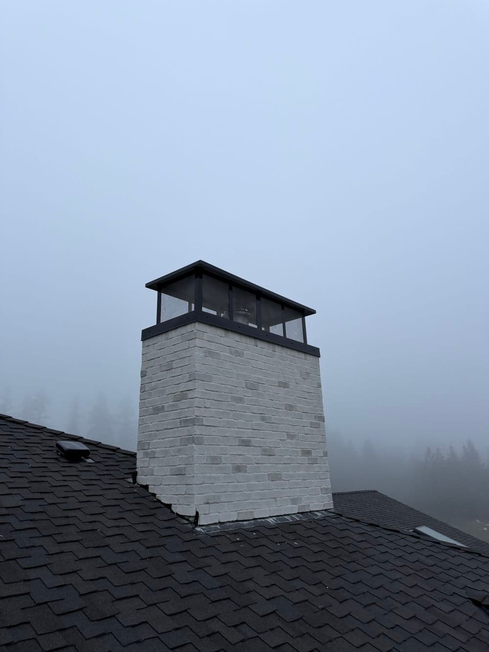 Chimney structure atop a dark shingle roof in a foggy landscape.