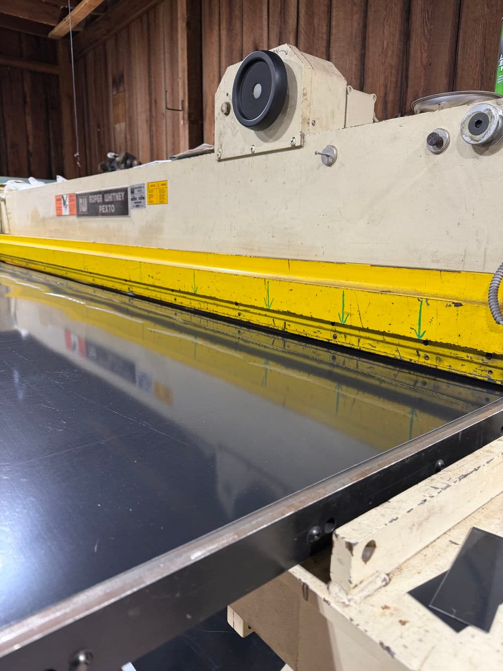 Industrial metal cutting machine with yellow guard, reflecting polished surface and wooden backdrop.