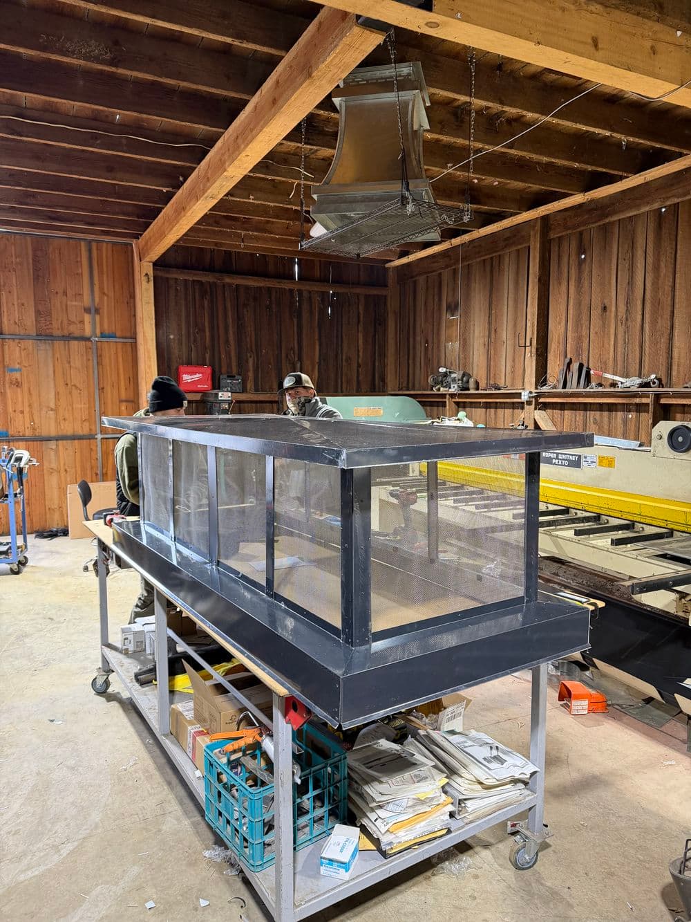 Two workers assembling a large glass display case in a wooden workshop.