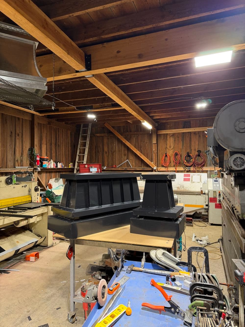 Workshop interior with wood beams, tools, and a black table under bright LED lights.