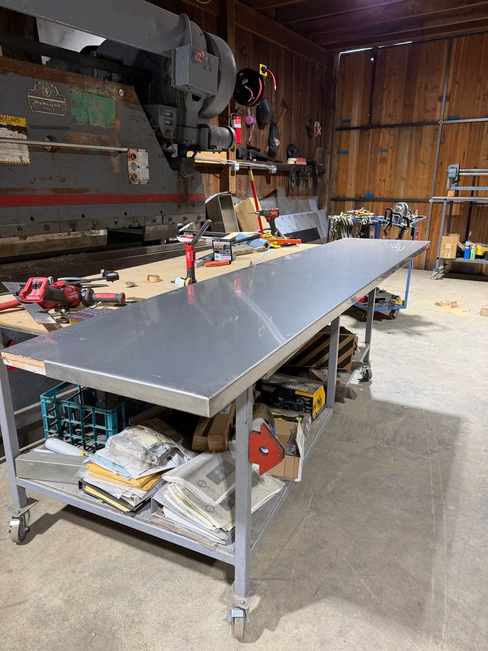 Steel workbench in a workshop with tools and materials on a concrete floor.