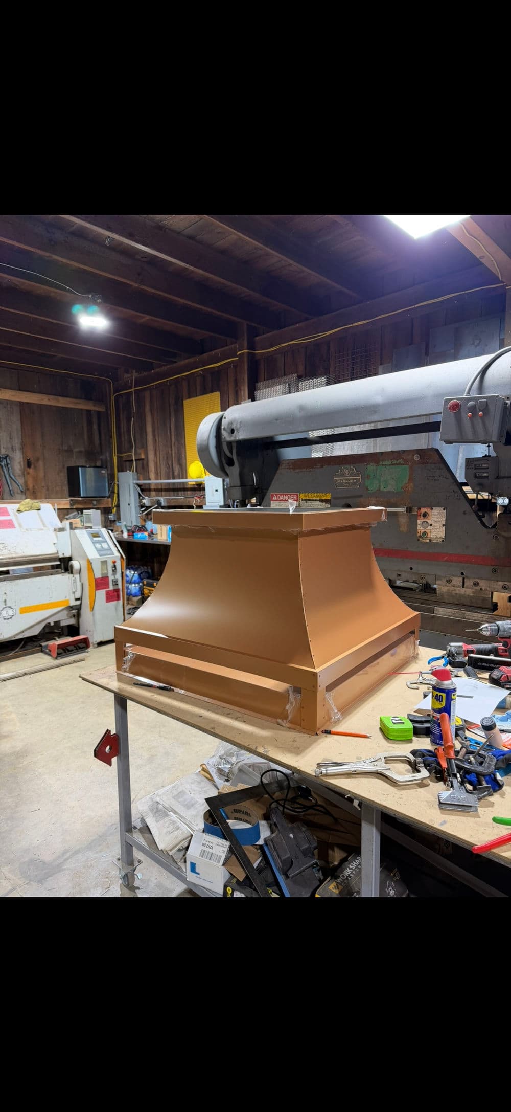 Home workshop with a copper-colored shelf prototype on a table, surrounded by tools.