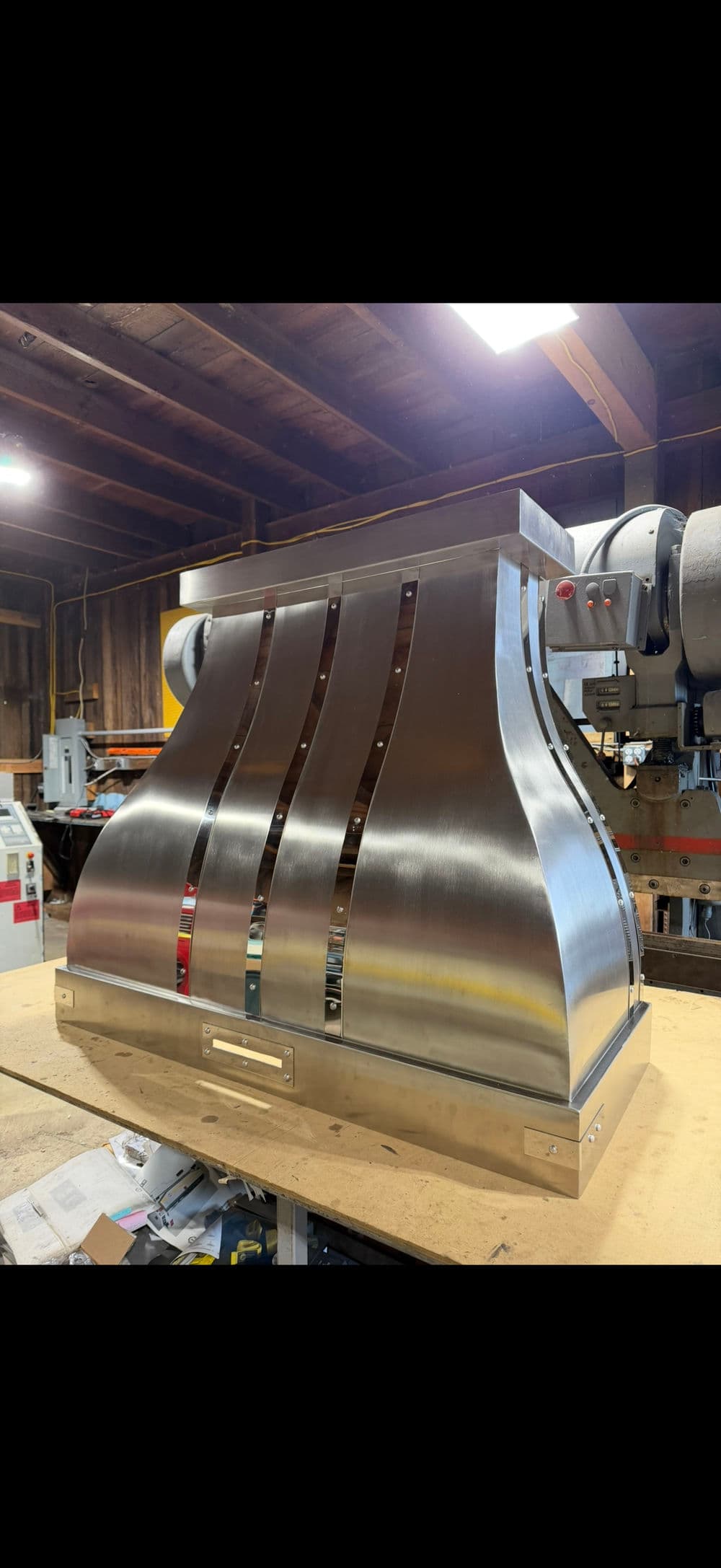 Stainless steel kitchen range hood with curved design, showcased in a workshop setting.