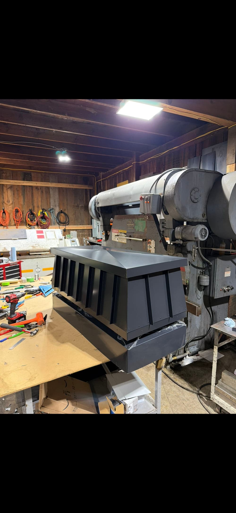 Industrial workshop with a large black metal fabrication piece and machinery in the background.