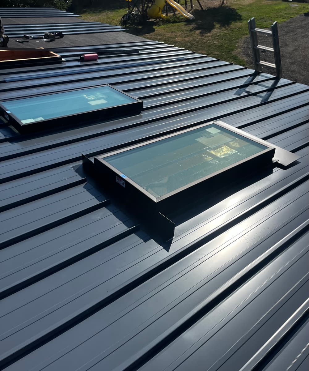 Skylights on a metallic roof under sunlight with tools in the background.